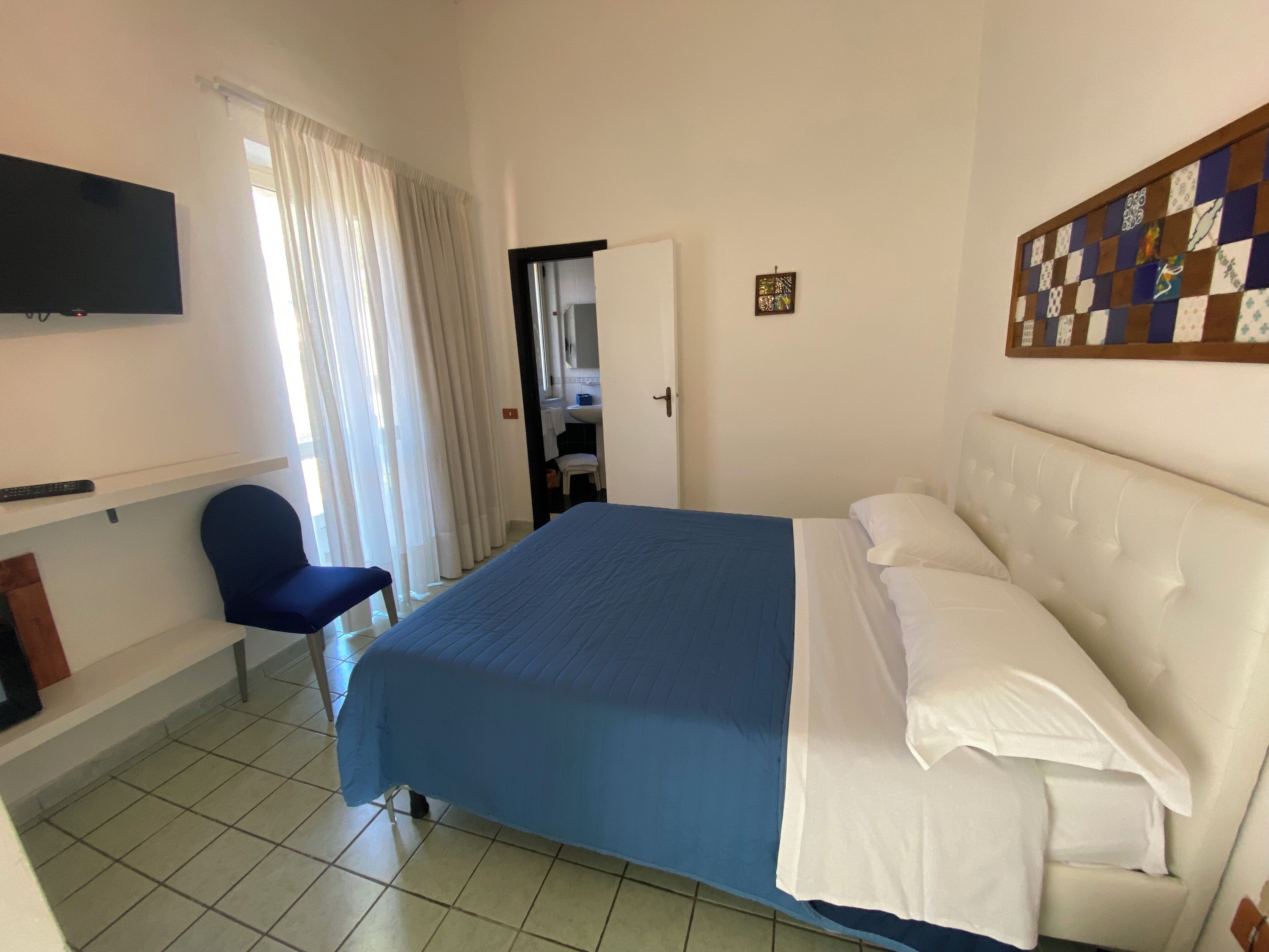 A bedroom with a bed, a chair, a TV, and a wall with a checkered pattern.