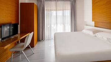 Una habitación de hotel moderna con una cama grande, un escritorio con silla, un televisor y una ventana con cortinas.