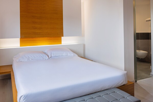 A modern bedroom with a large bed, a wooden accent wall, and a glass shower door. - Precise House Montaperti Siena (Asciano)