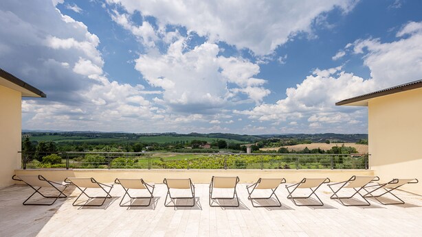 Una terraza con varias tumbonas y una vista panorámica de campos verdes y colinas.