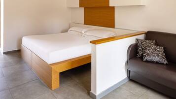 Une chambre moderne avec un cadre de lit en bois, une literie blanche, une tête de lit en verre et un canapé marron agrémenté de coussins à motifs.