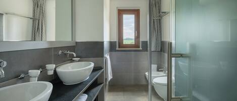 A modern bathroom with two large sinks, a glass shower enclosure, and a window providing a view of the outdoors.
