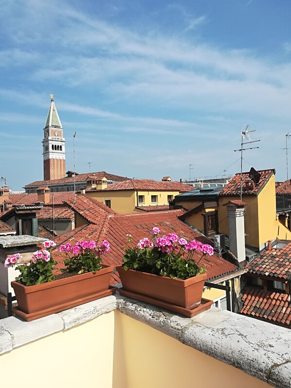 Una azotea con tejas de terracota, macetas de terracota y una vista despejada de una torre histórica al fondo.