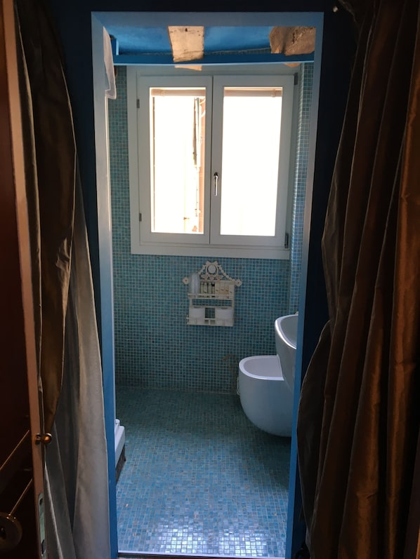 A bathroom with a blue tiled floor, a white toilet, and a window above the sink.