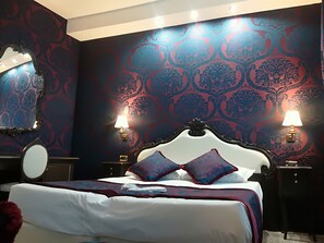 A bedroom with a large bed, ornate headboard, two bedside lamps, a round mirror, and patterned wallpaper. - Antica Venezia (Venice)