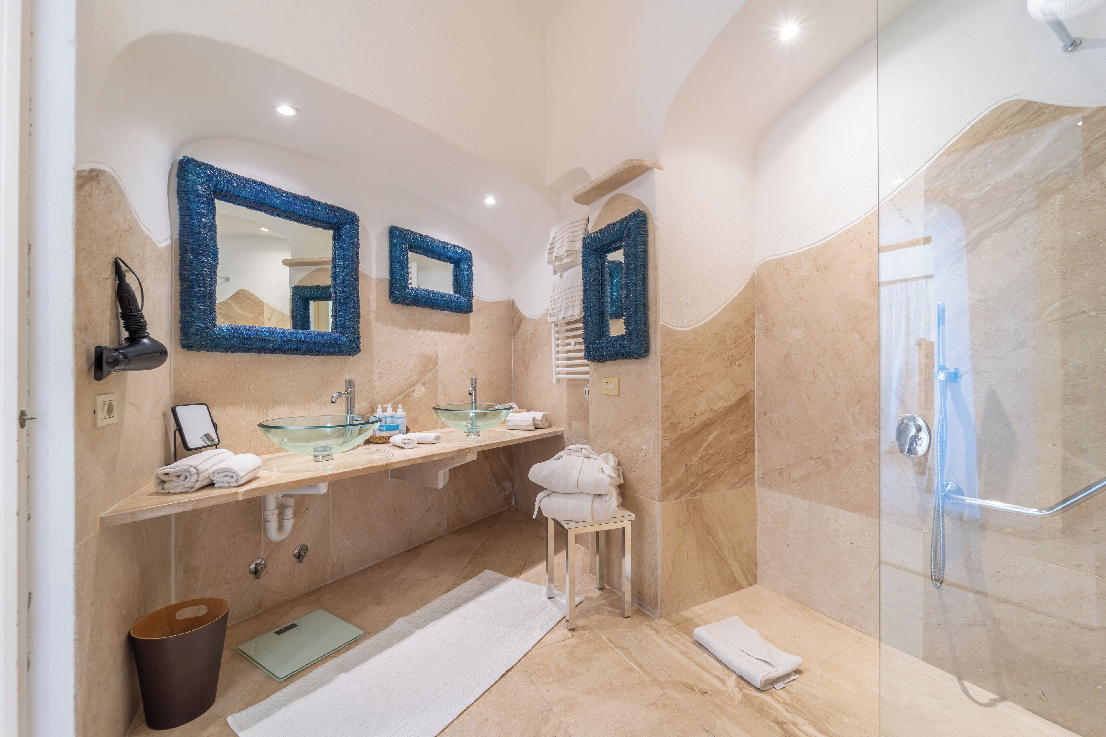 Une salle de bain moderne avec une douche en verre, des murs en marbre beige et un grand miroir.