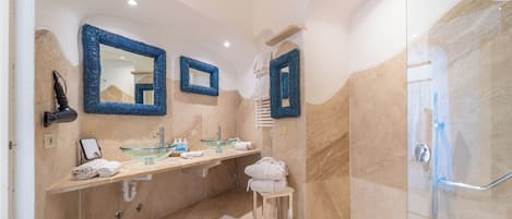 A modern bathroom with a glass shower, beige marble walls, and a large mirror.