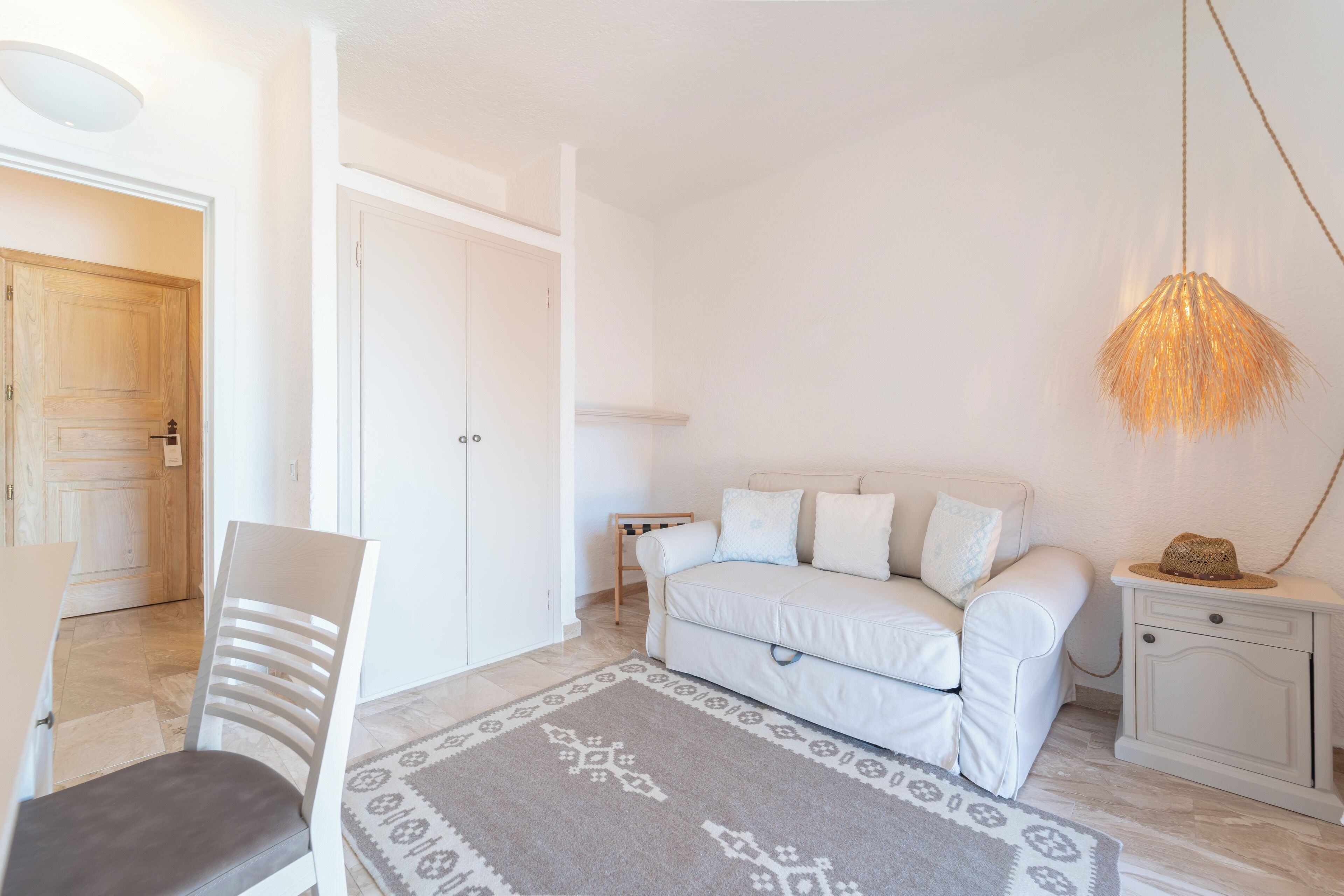 Une pièce blanche avec un canapé, un fauteuil, une table de chevet et un luminaire suspendu.