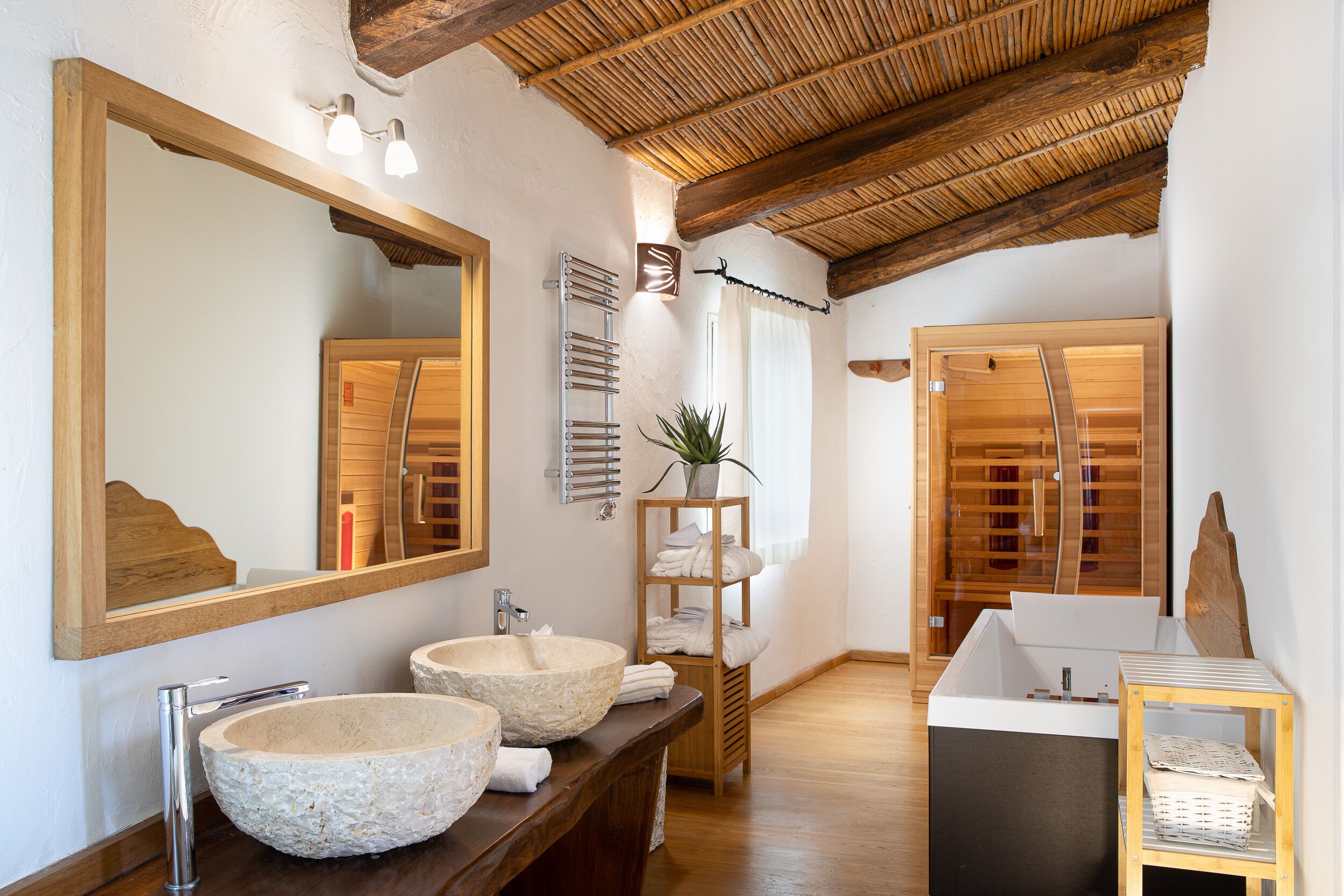 A modern bathroom with a wooden vanity, two stone sinks, a large mirror, and a wooden ceiling.