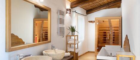 Un baño moderno con tocador de madera, dos lavamanos de piedra, un espejo grande y techo de madera.