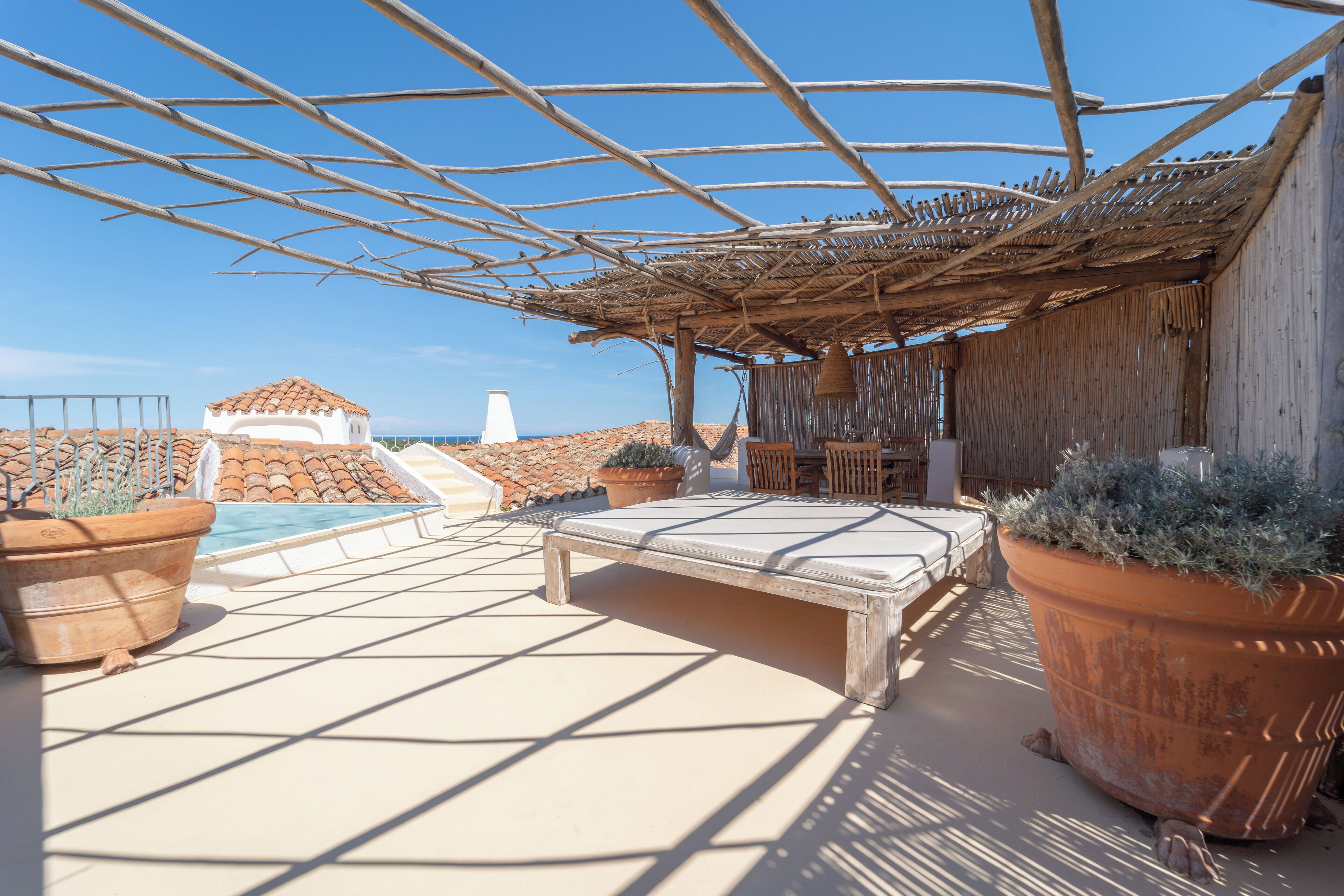 Un espacio al aire libre iluminado por el sol con piscina, macetas de terracota y una estructura de pérgola.