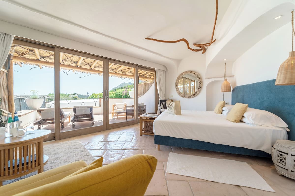 Une chambre dotée d’un grand lit, d’un balcon avec mobilier d’extérieur et offrant une vue sur le paysage.