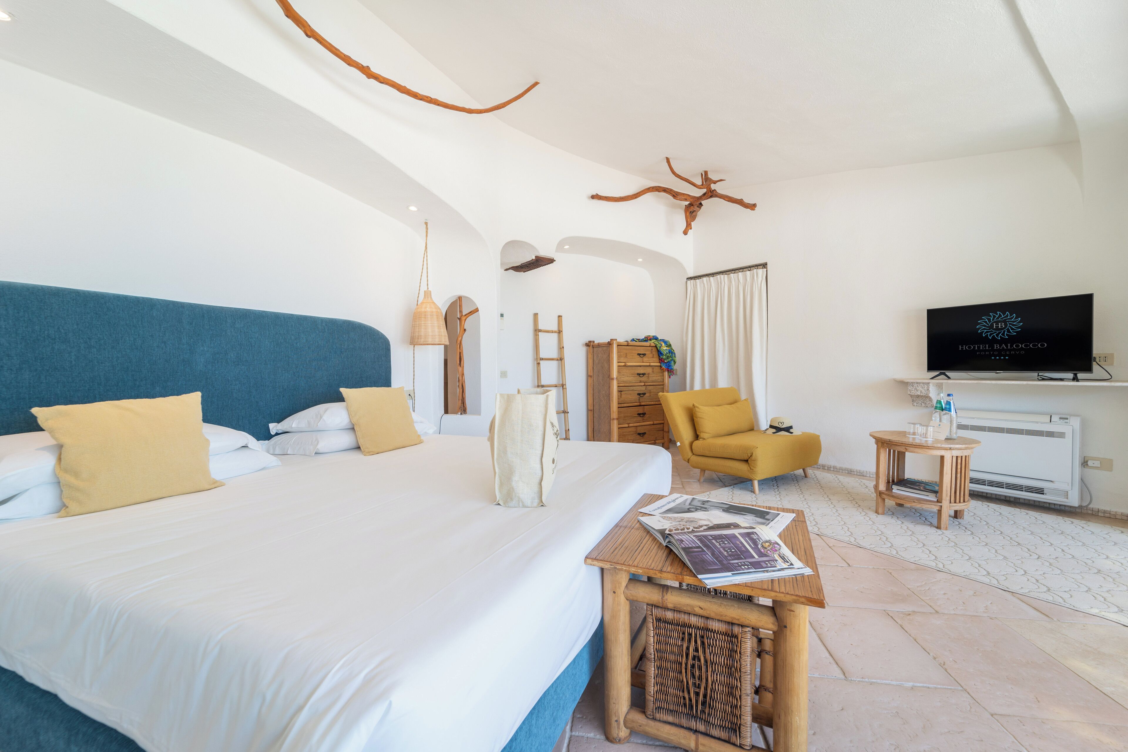 A hotel room with a large bed, a television, a small table, a chair, and a decorative antler on the wall.