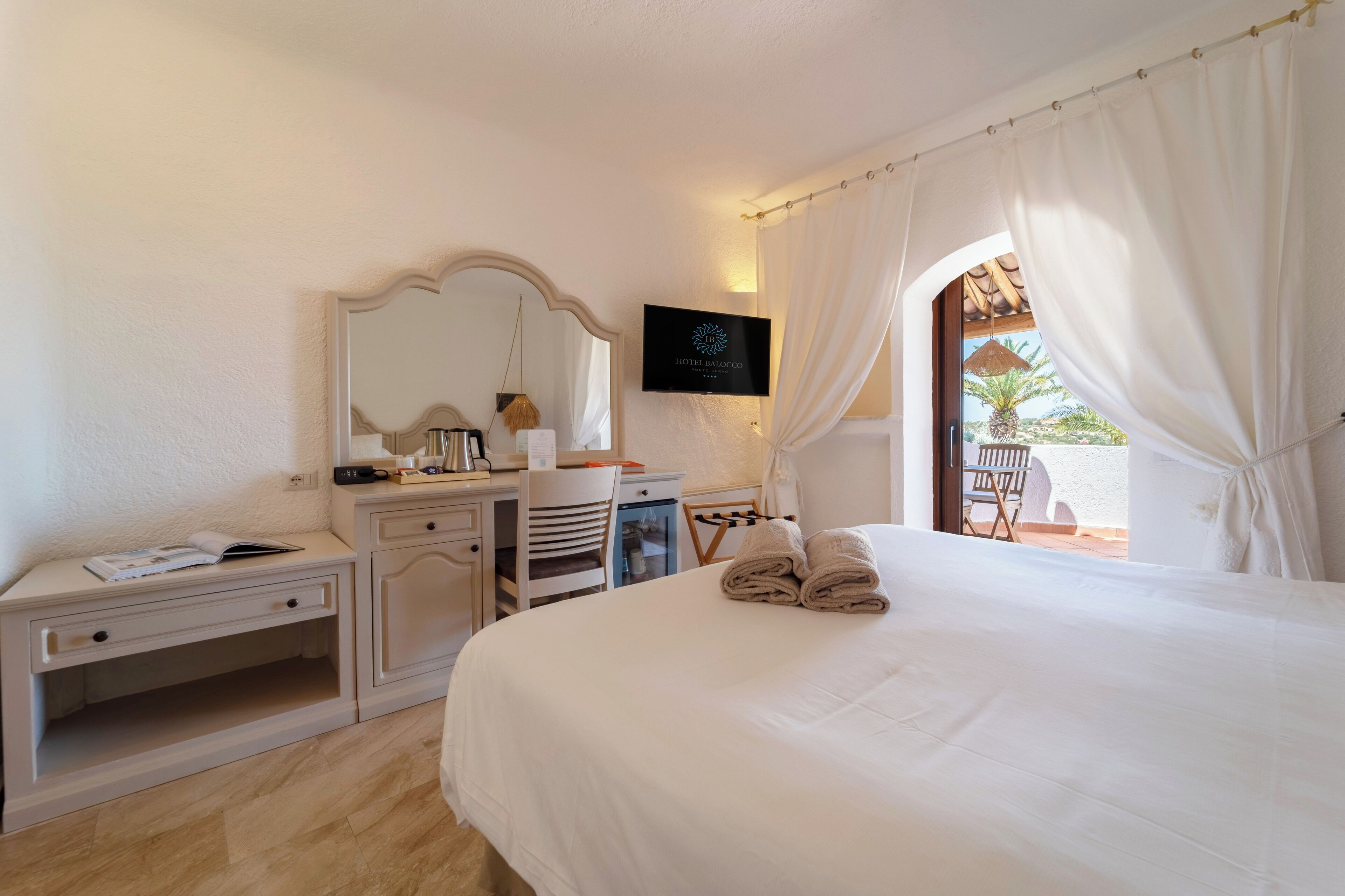 Habitación de hotel con cama, escritorio, silla, televisión y vistas al exterior.