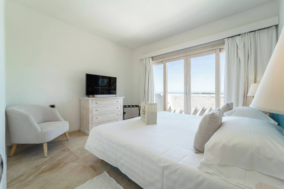 Une chambre d’hôtel avec un lit, une télévision, une chaise, une commode et une fenêtre avec des rideaux.