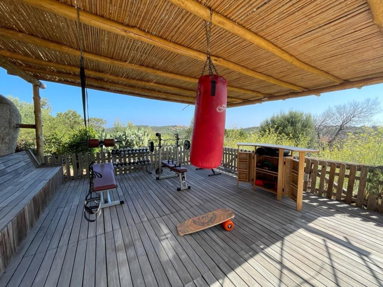 An outdoor gym with exercise equipment, a punching bag, and a skateboard.