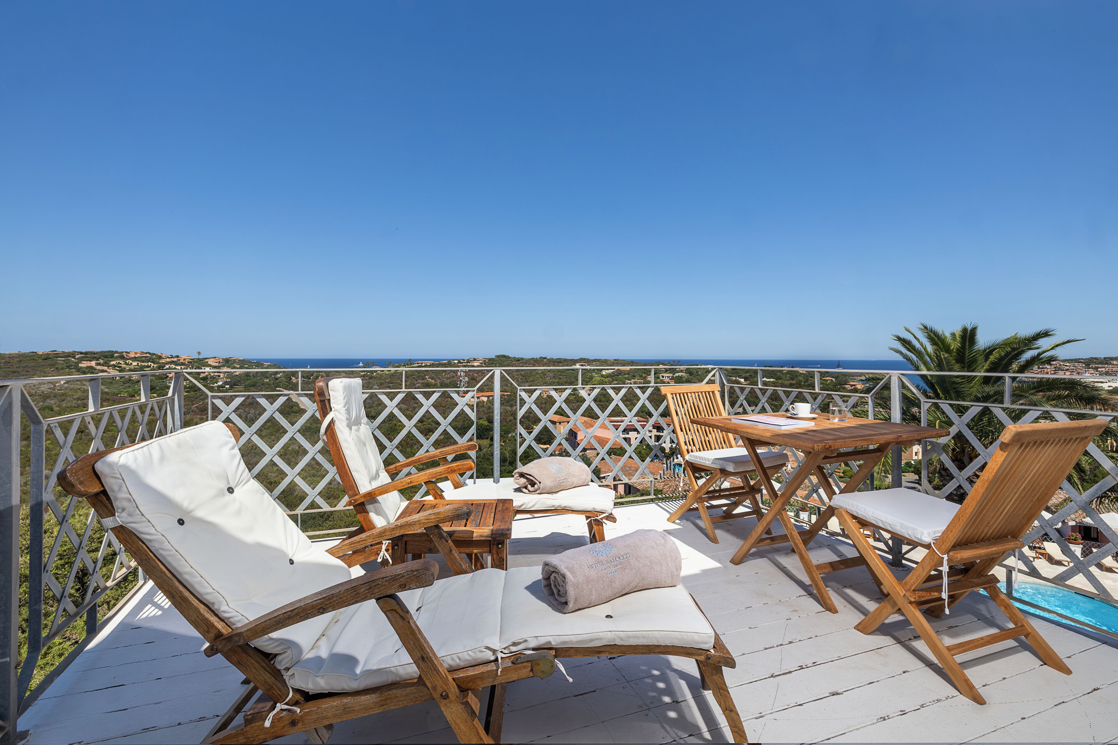 Eine Holzterrasse mit Liegestühlen und einem Tisch mit Blick auf einen Strand und das Meer.