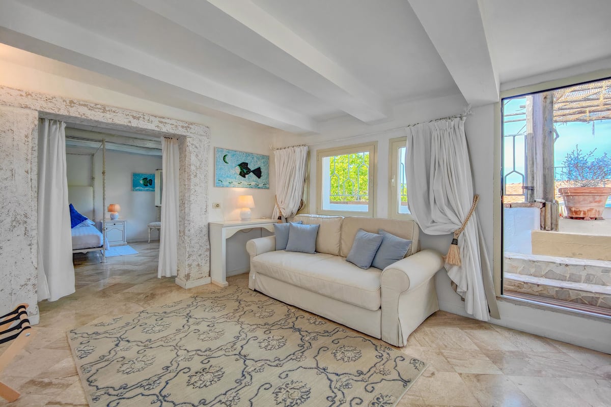 Un salon spacieux avec un canapé beige, un tapis à motifs et une vue sur la verdure.