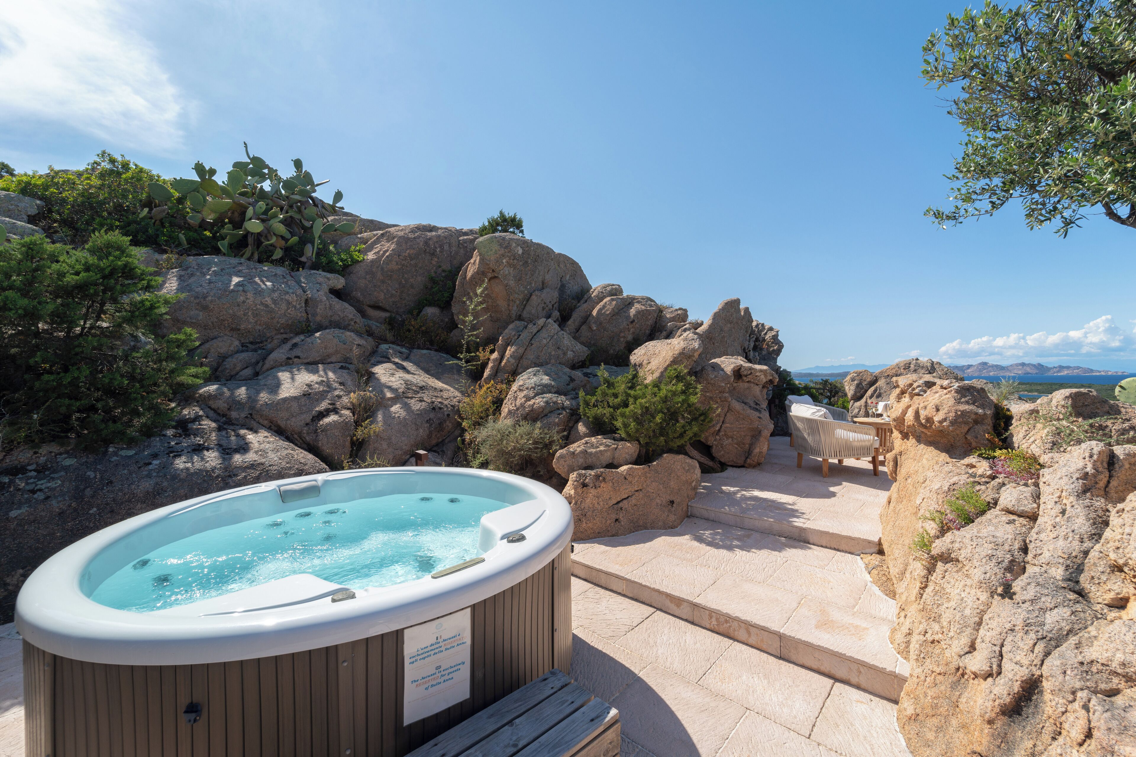 A hot tub surrounded by rocks and a wooden deck with a view of the mountains.