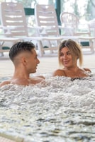 Um casal em uma banheira de hidromassagem, com espreguiçadeiras ao fundo.
