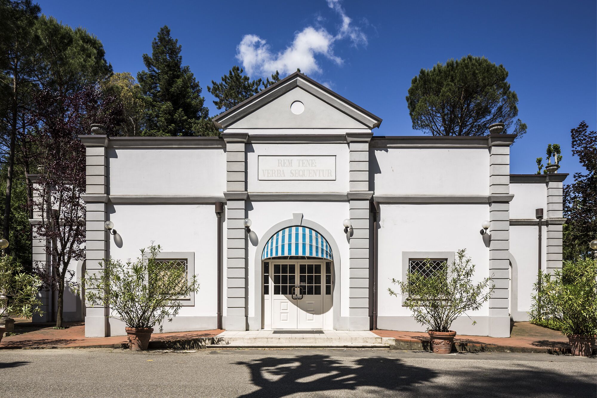 A building with a white facade, a central entrance with a blue and white striped awning, and a sign above the entrance.