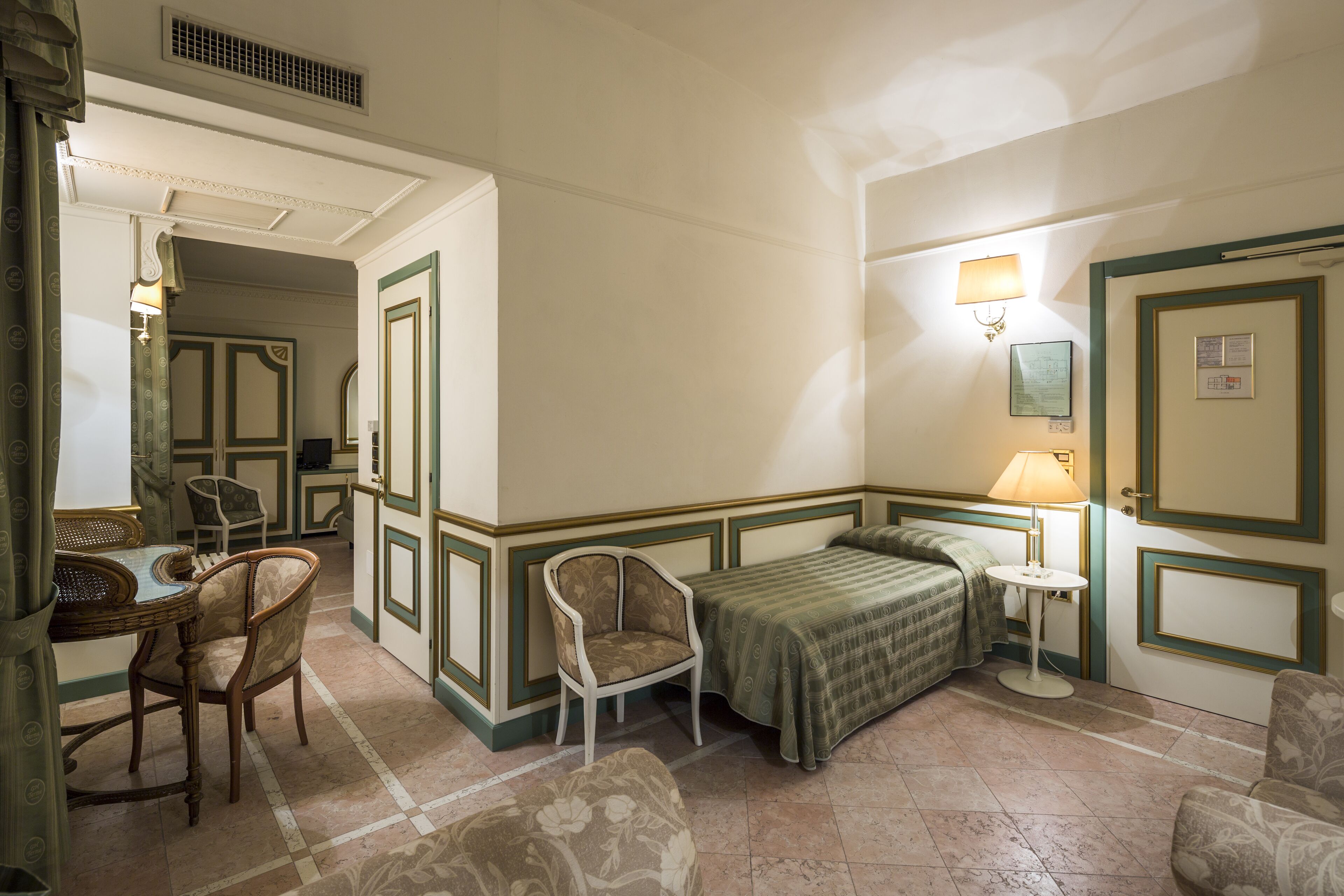 Una habitación de hotel con una cama, dos sillas, una mesita y una lámpara.