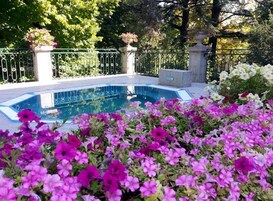 Piscina cercada por grade de metal e canteiros com flores rosa e brancas.