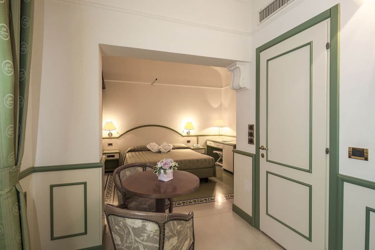 A hotel room with a bed, bedside lamps, a table with a vase, and a chair.