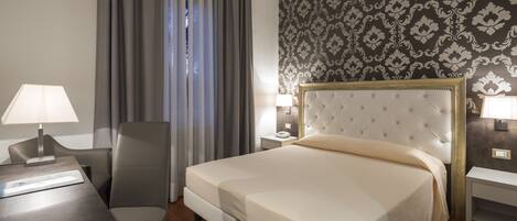 Habitación de hotel ordenada con una cama grande, un escritorio, una silla y una mesita de noche con lámparas.