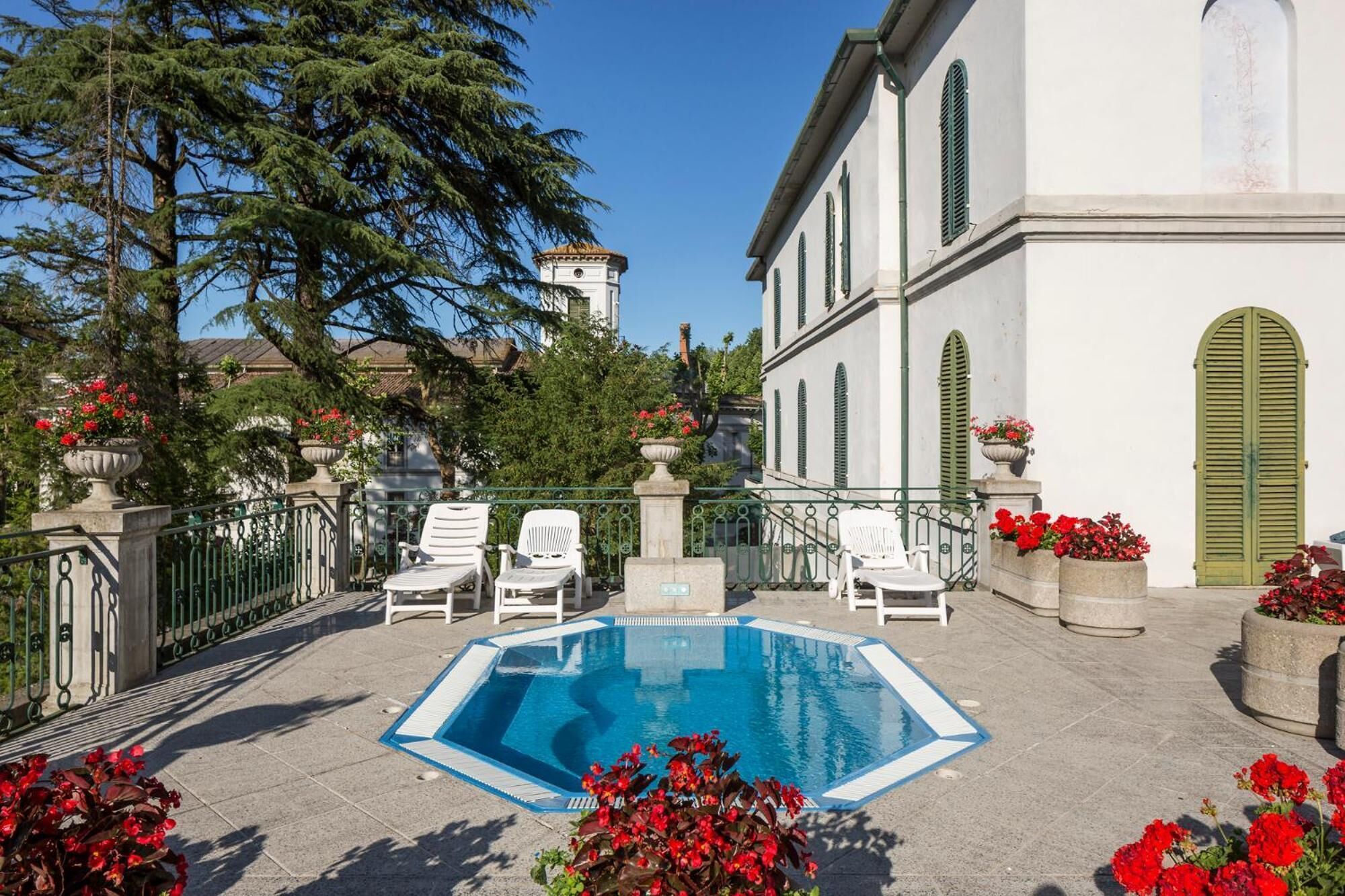 A pool area with lounge chairs, a clear blue pool, and red flowers.