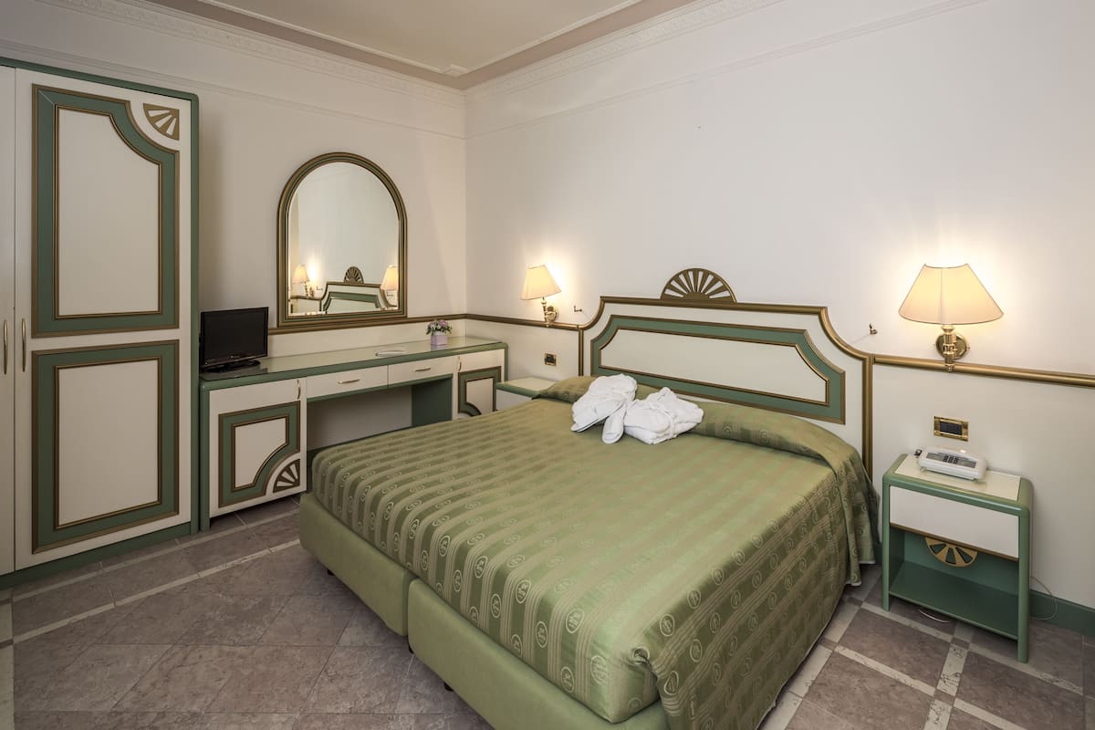 A hotel room with a bed, a desk, a dresser, a mirror, and two bedside lamps.