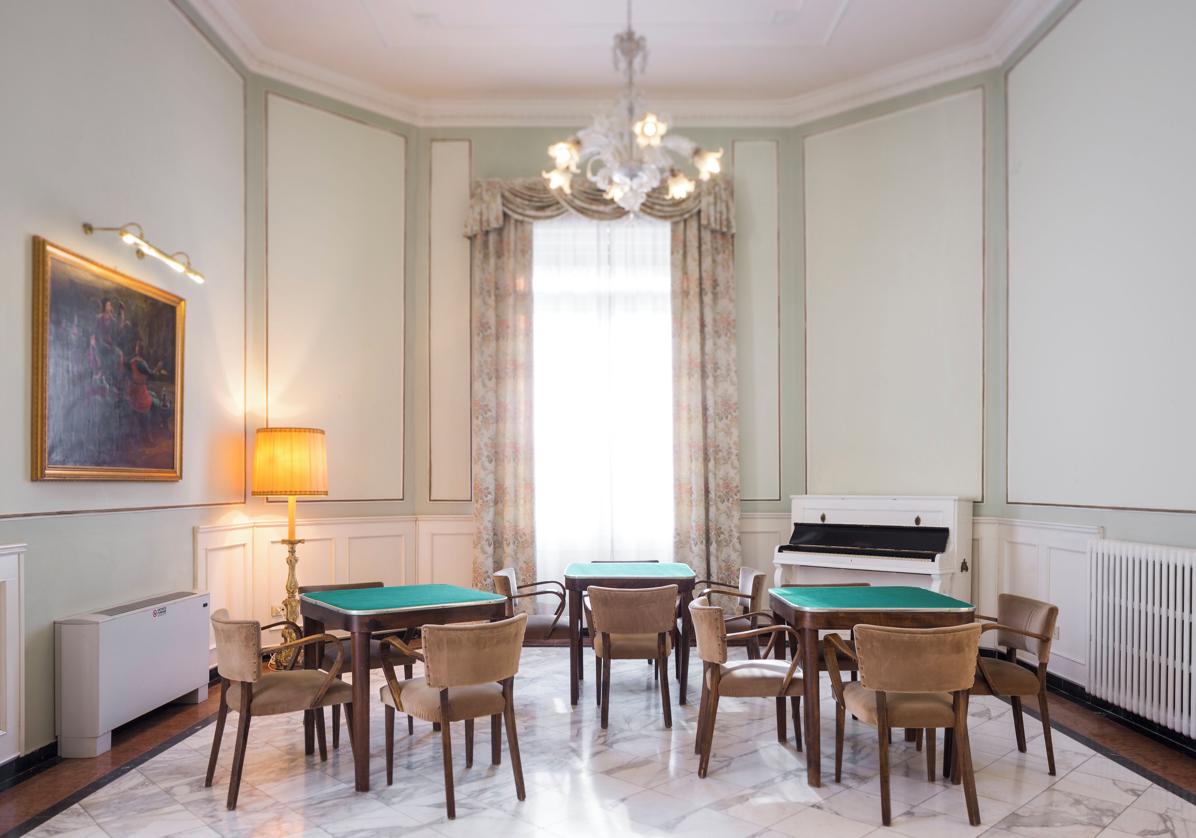 Una stanza con tavolo da biliardo, sedie, un pianoforte, un termosifone e un lampadario.