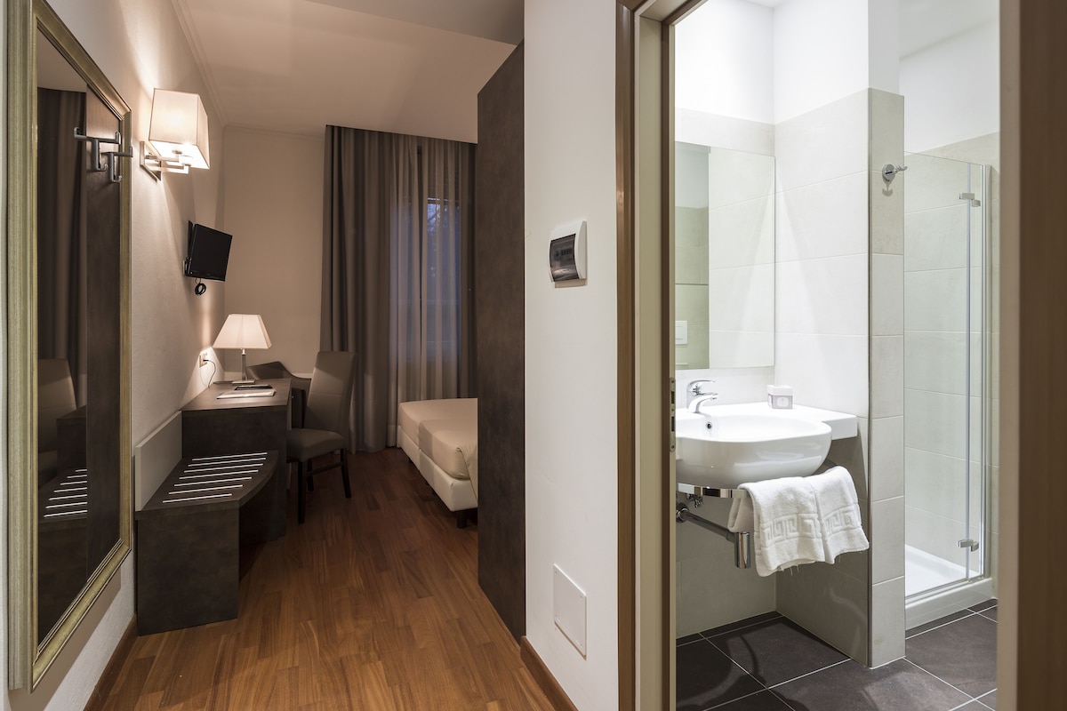 A hotel room with a desk, chair, sofa, and a shower area.