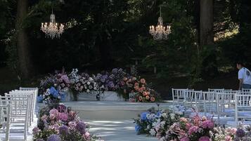 Un pasillo nupcial al aire libre con sillas blancas, arreglos florales y candelabros.