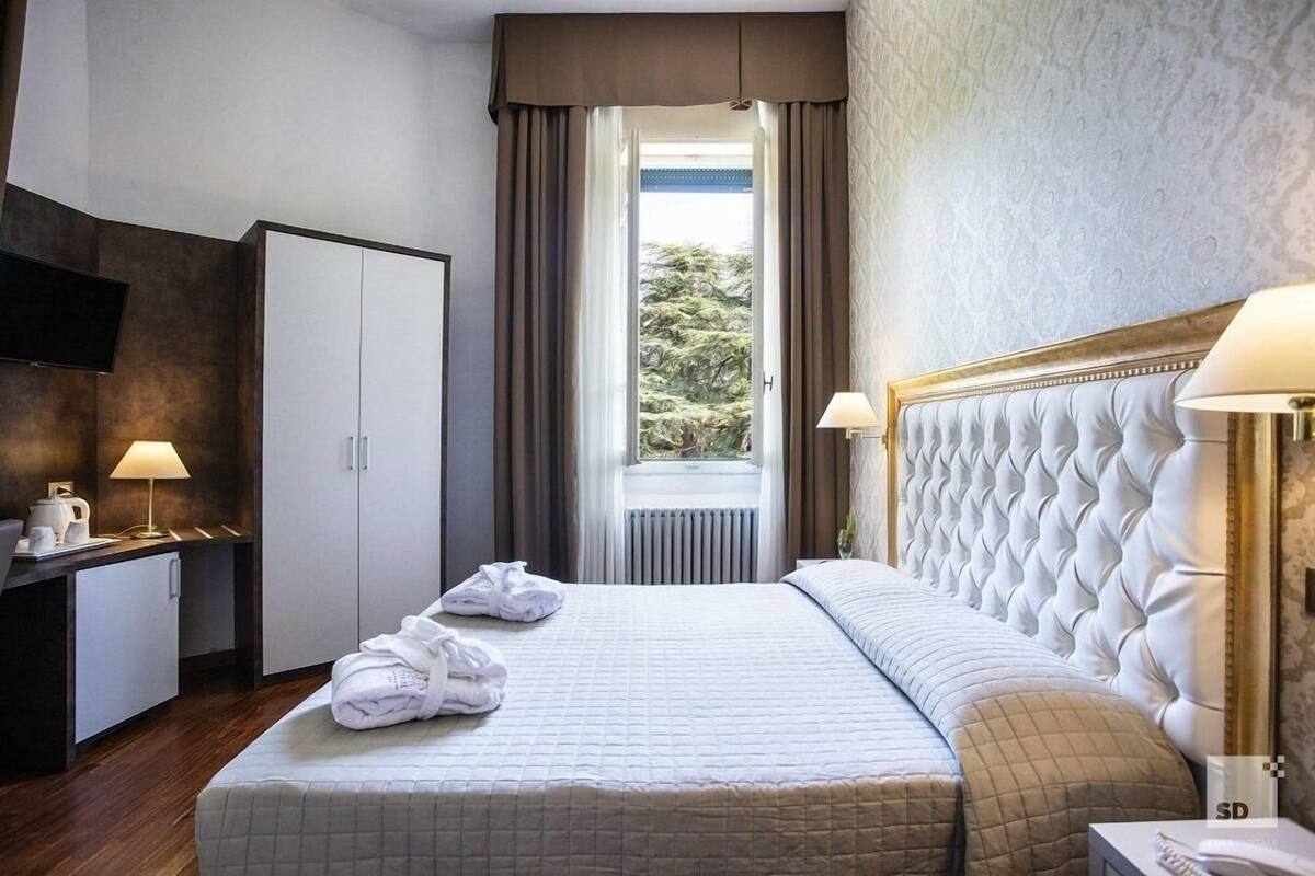 A hotel room with a bed, a desk, a television, and a window with curtains.