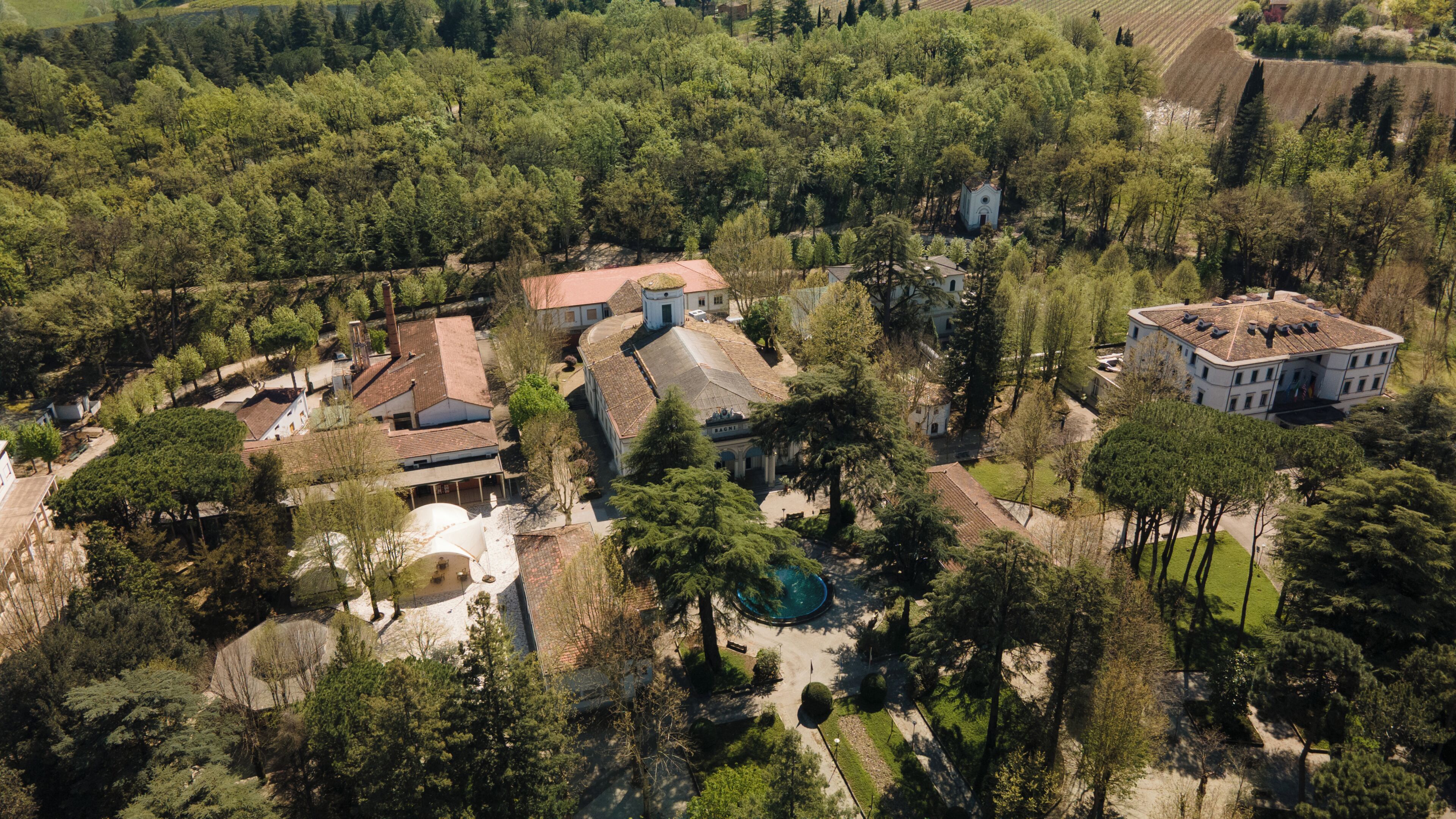 An aerial view of a historic estate with multiple buildings, a central courtyard, and surrounding forested areas.