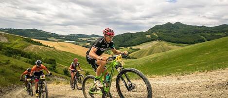 A group of cyclists on a dirt path with a scenic view of rolling hills and a cloudy sky.