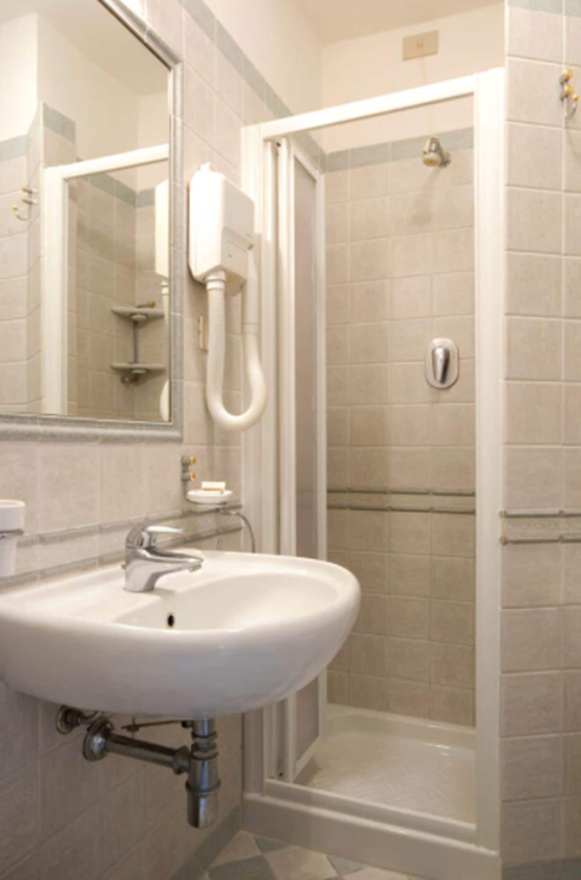Un baño con lavamanos blanco, espejo y cabina de ducha con mampara de vidrio.
