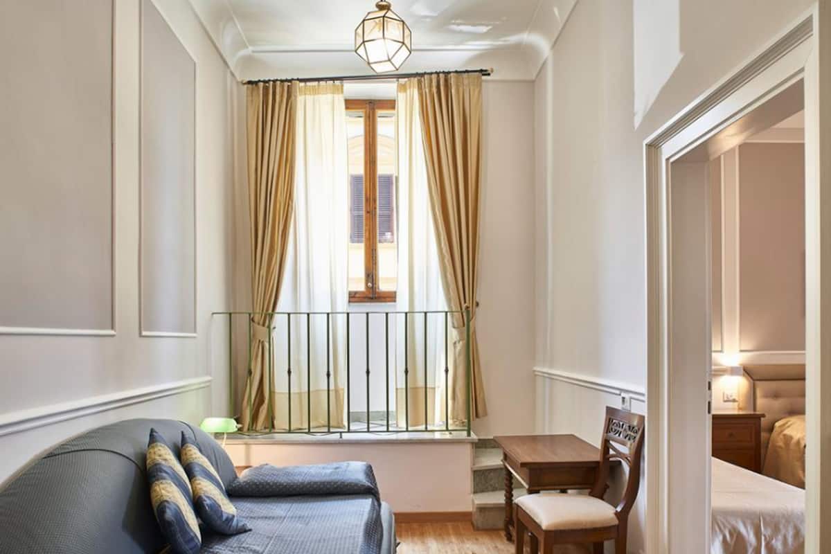 Una habitación pequeña con cama, una mesita y ventana con cortinas.