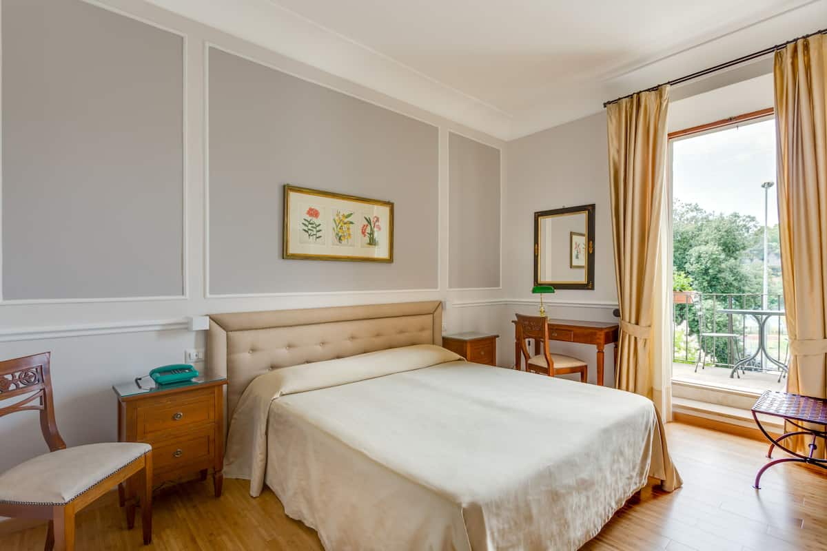 Un dormitorio con una cama grande, una mesita de noche, una silla, un escritorio y una ventana con cortinas.