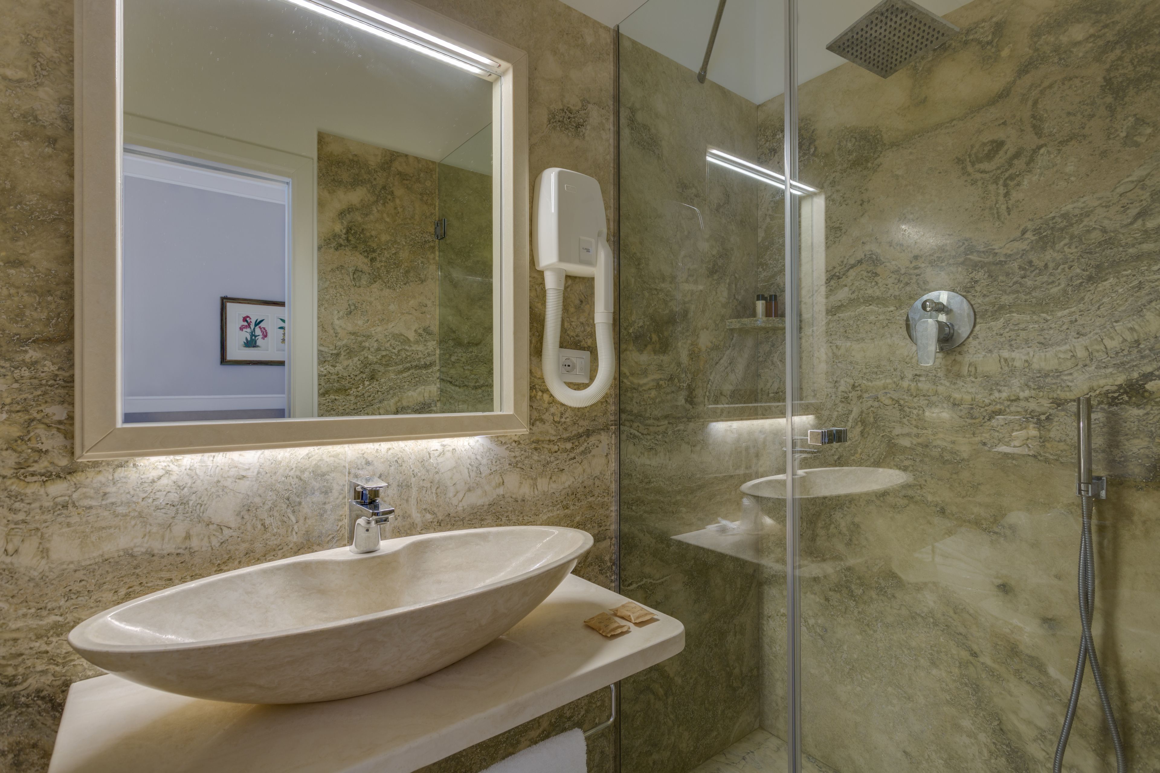 Un baño con un lavamanos ovalado grande, un espejo, un cabezal de ducha de mano y una pared de mármol.
