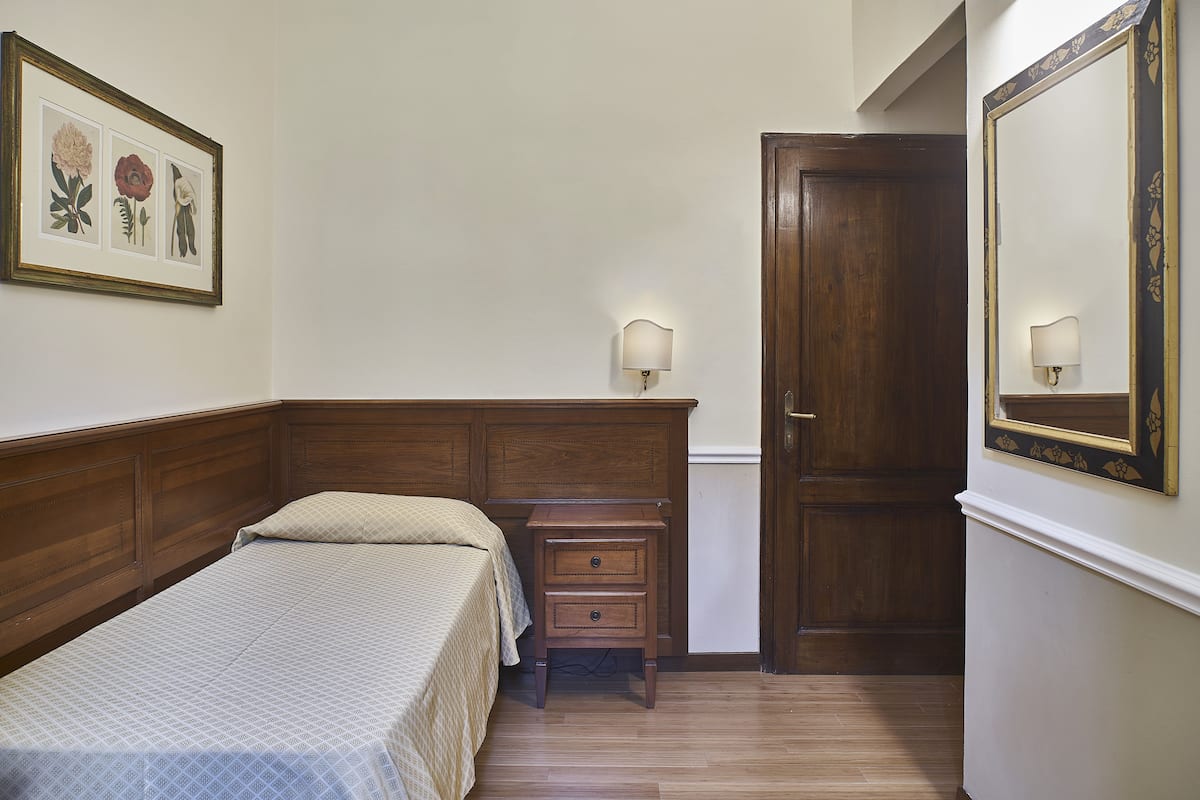 Un dormitorio con cama de madera, una mesita de noche con cajones, una obra de arte floral enmarco y una puerta con espejo.