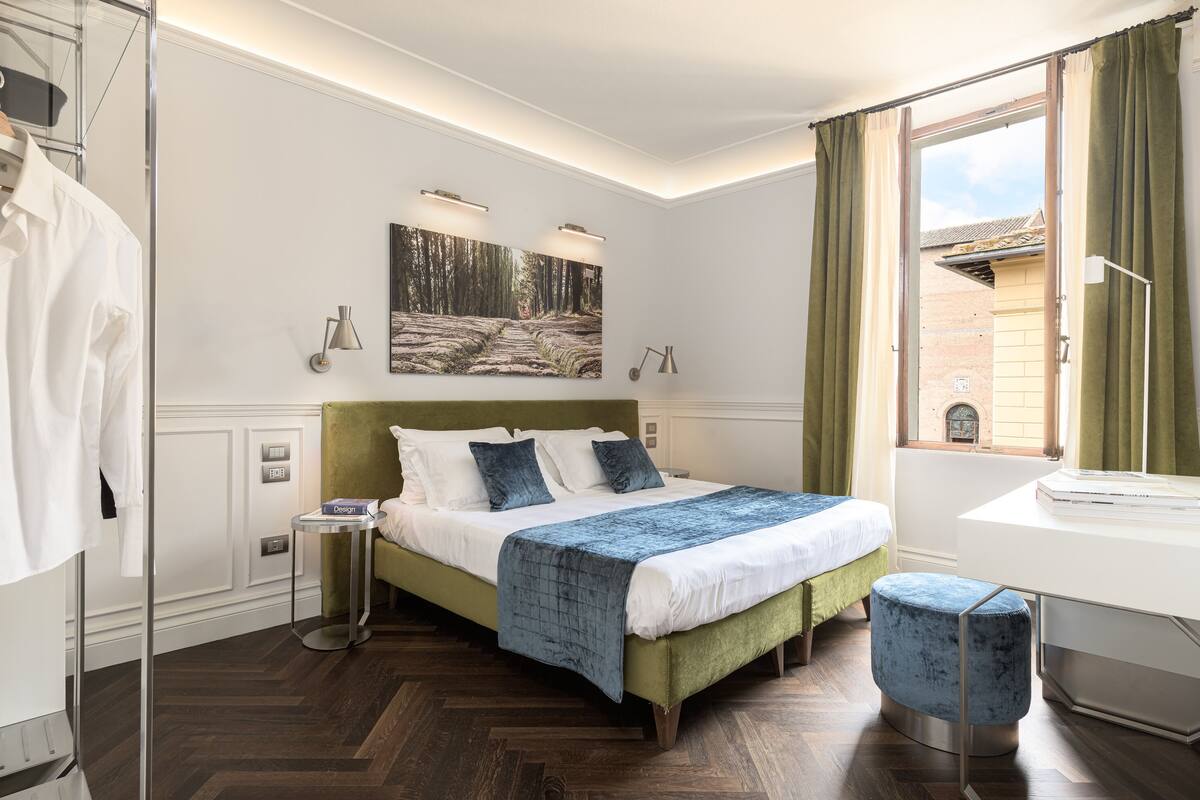 Un dormitorio moderno con una cama tapizada en verde, una mesita de noche, un ventanal con cortinas y un cuadro sobre la cama.