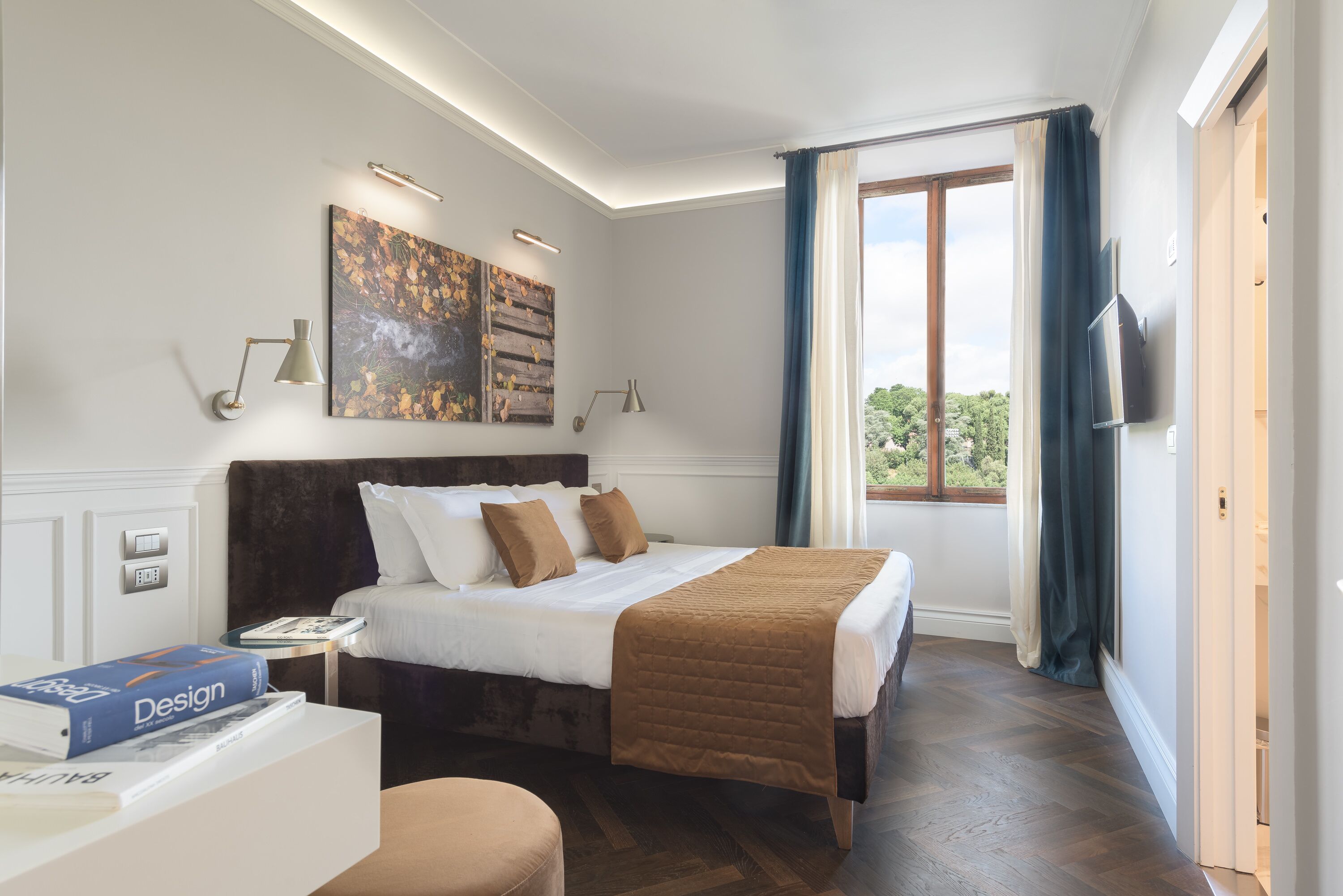 A modern bedroom with a large bed, a bedside table with a book, a wall-mounted TV, and a window with curtains.