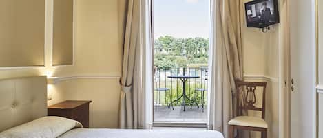A hotel room with a bed, a TV mounted on the wall, a chair, and a balcony with a table and chairs.