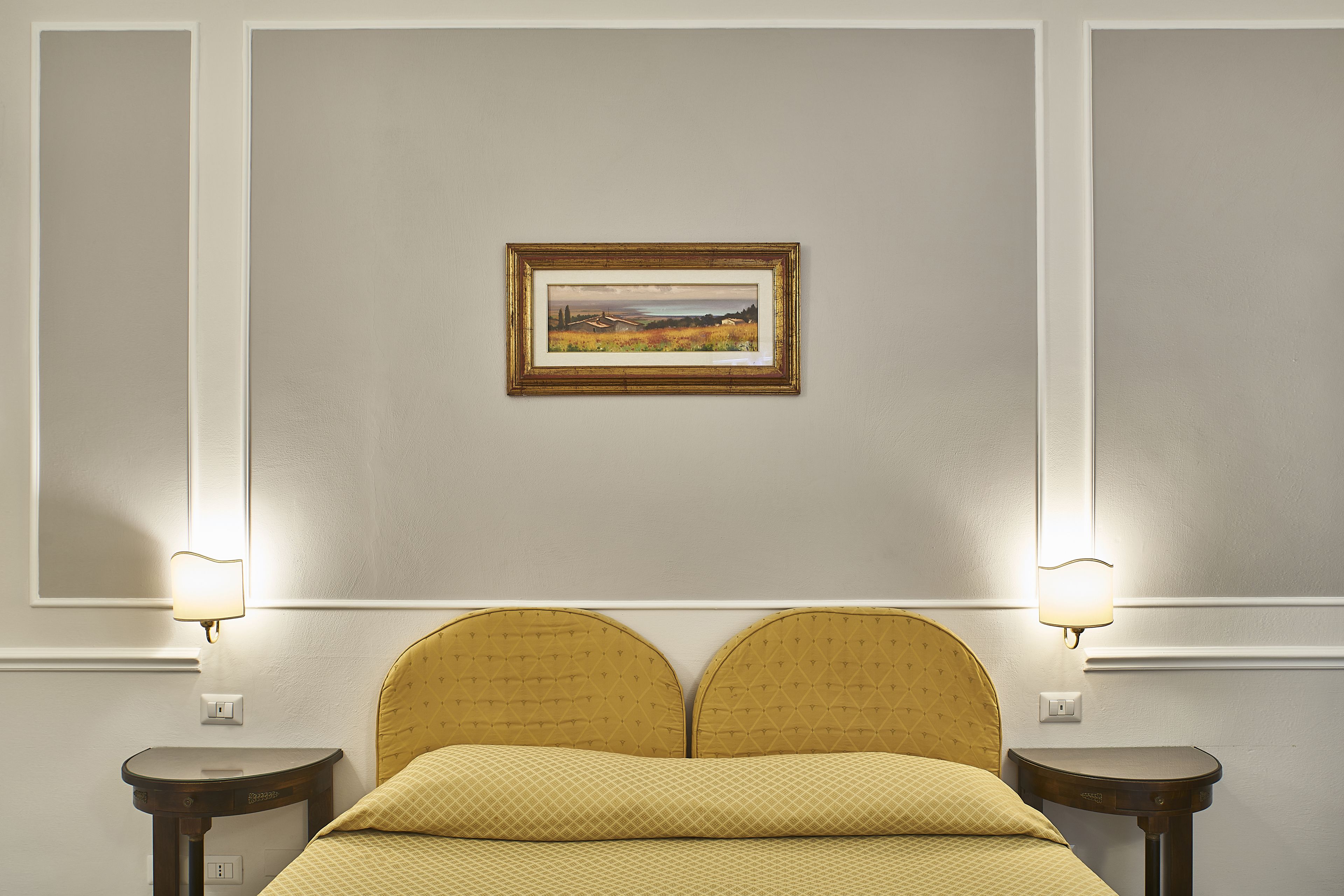 A hotel room with a bed, two bedside tables, a wall-mounted picture, and two wall sconces.