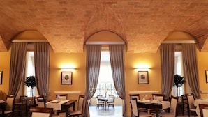 Comedor con arcos de techo de ladrillo, mesas dispuestas con manteles blancos y cuadros en las paredes.
