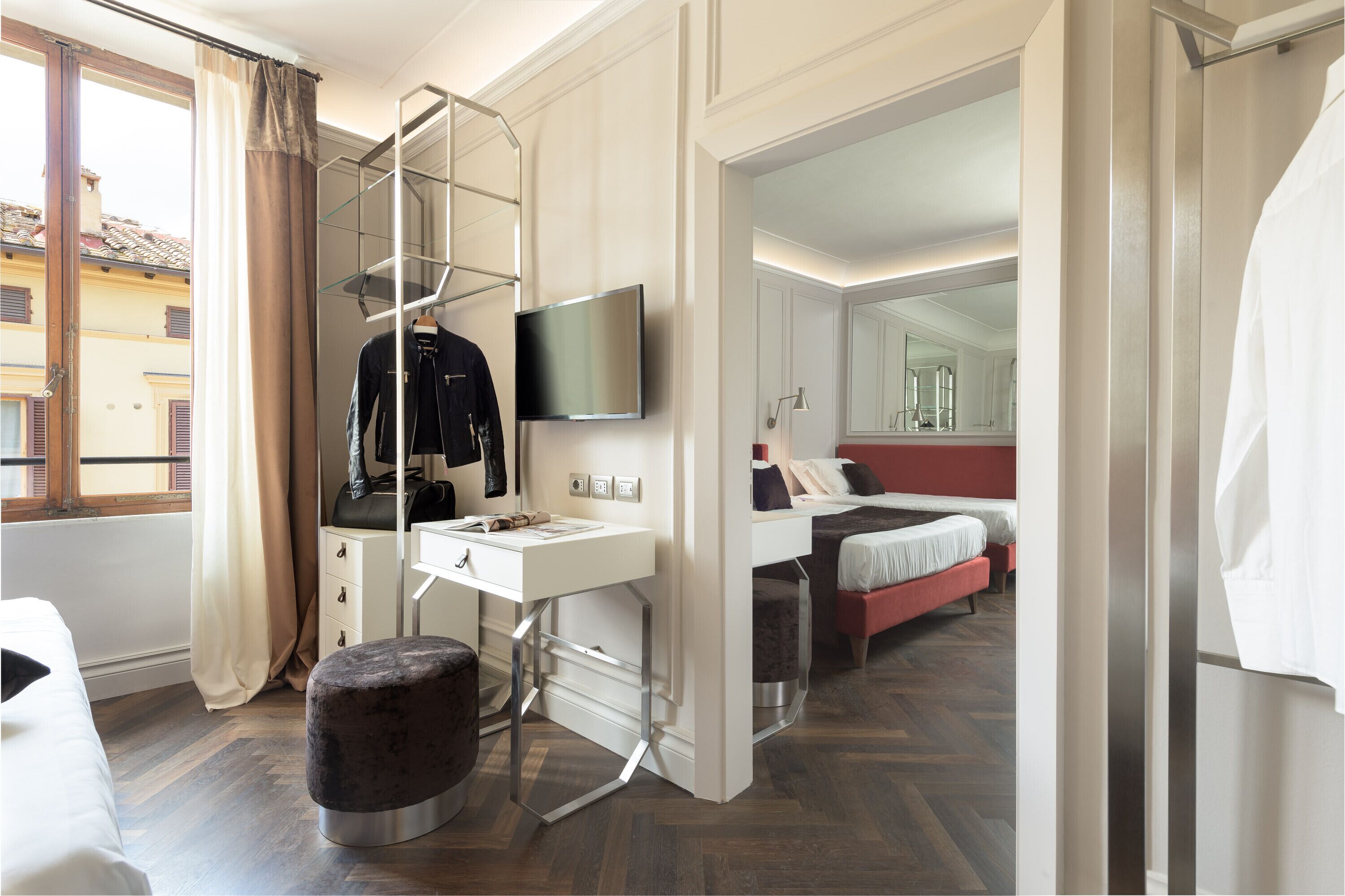 A modern hotel room with a bed, a desk, a TV, and a window with curtains.