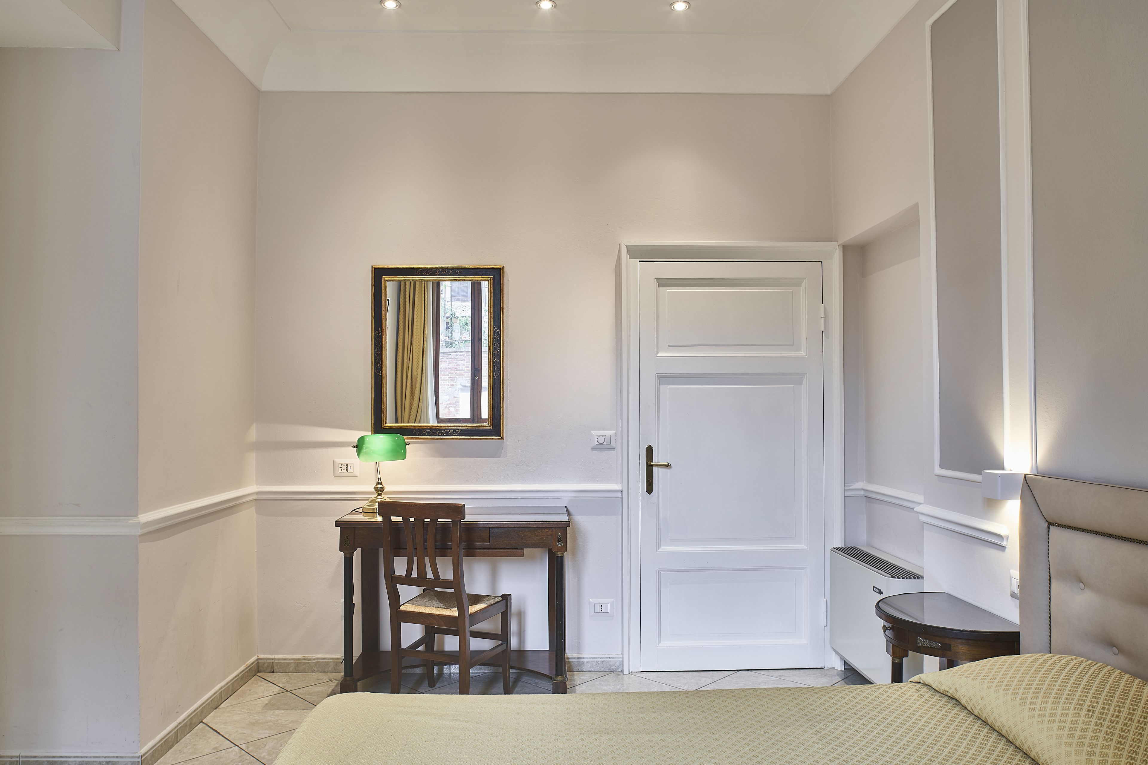 Une chambre à coucher avec un lit, un bureau et une chaise, une porte et un miroir au mur.