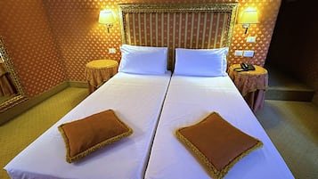 Un lit double avec du linge de lit blanc et deux oreillers marron, une table de chevet avec une lampe et un papier peint à motifs.
